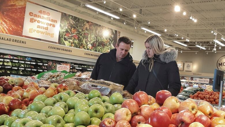 Two people shop in a market's produce section.