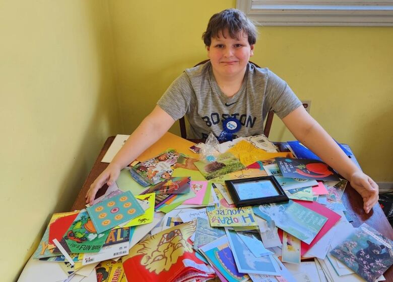 A boy sitting with hundreds of birthday cards in front of him. 