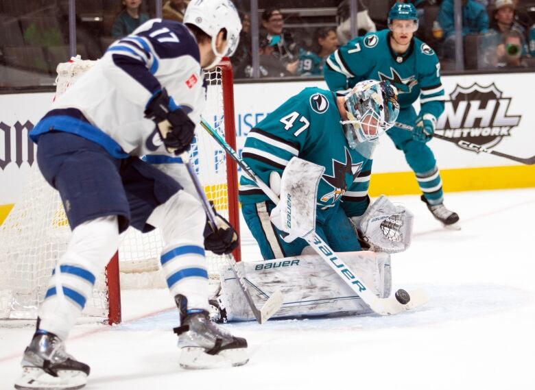 San Jose's goaltender drops to his knees to make a save as a Winnipeg player looks for a rebound.