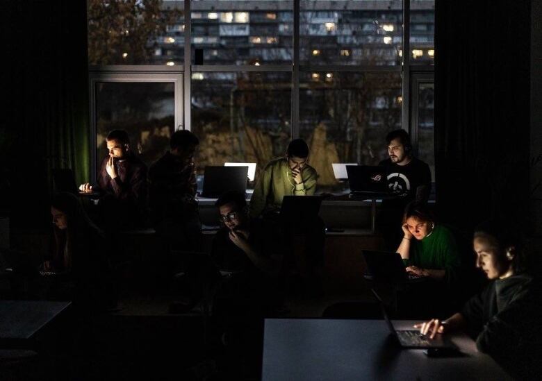 A group of people work on laptops at desks in a dark office building.