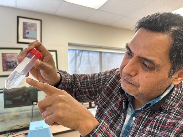 A man holds up a test tube and points at a spot in it.