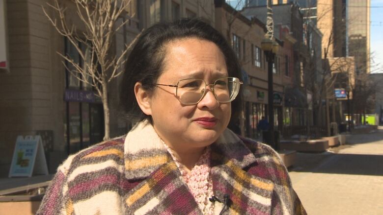 A woman with black hair and glasses wears a red, yellow and white pea coat.