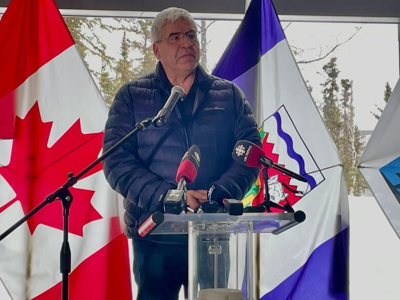 A man stands in front of a podium with a Canadian and a Northwest Territories flag behind him.