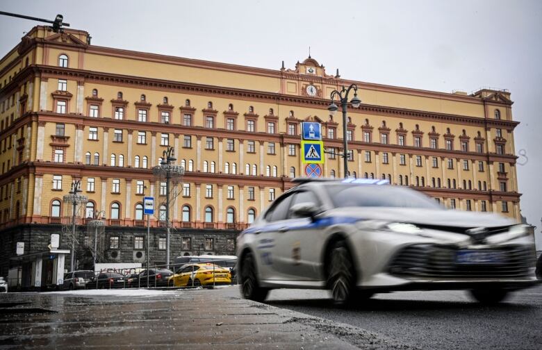 A vehicle is shown moving in the foreground with a wide, low-rise building seen in the background.