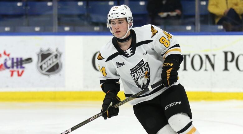 A hockey player wearing a white, yellow and black uniform holds a hockey stick while skating.