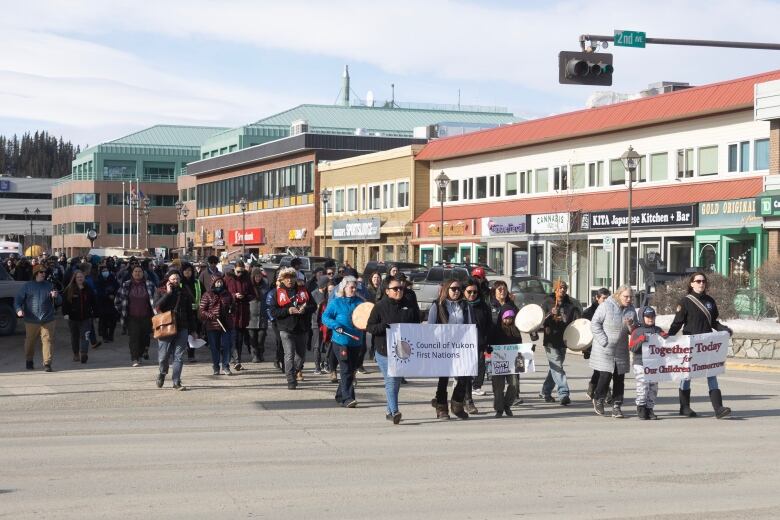 Crowd walking down street, carrying banner.