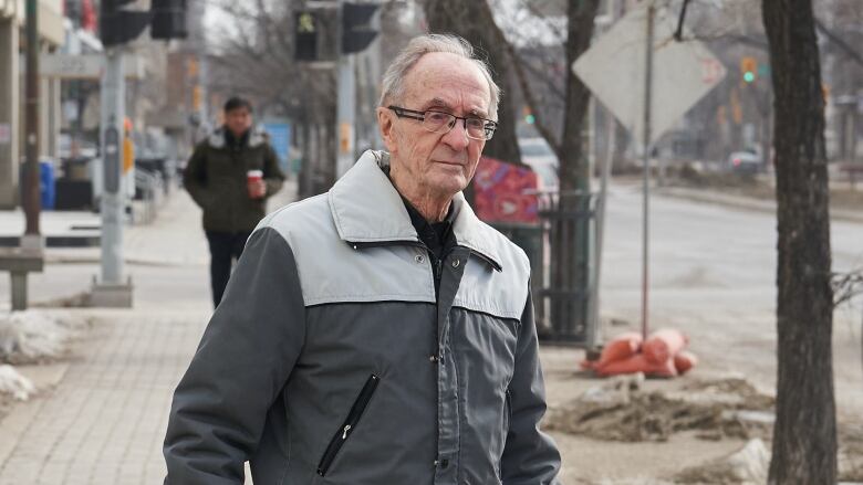 A man in a grey coat walks on a sidewalk.