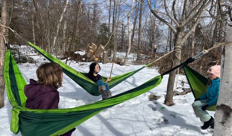 Three kids in snow gear play in outdoor hammocks in the snow