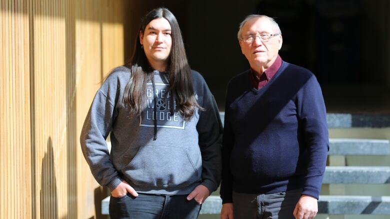 A young man stands next to his elder language teacher in a University hallway 