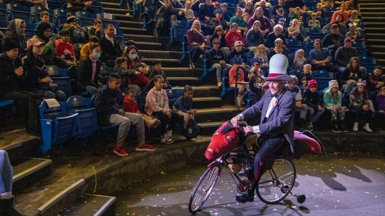 A man rides a bicycle dressed up like a horse wearing a silly cowboy hat.