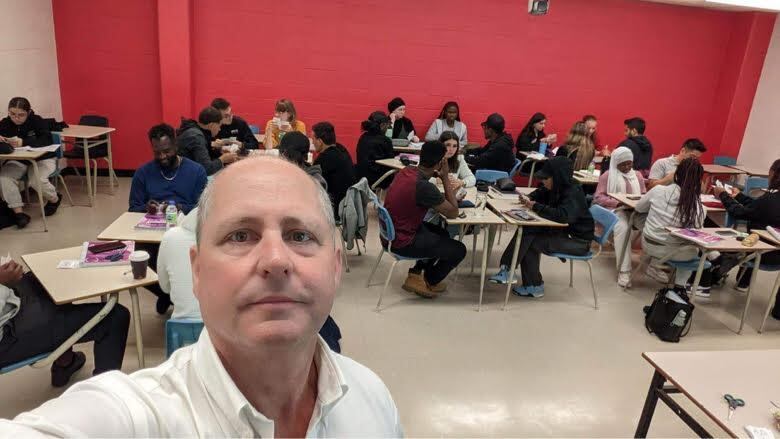 A teacher stands in front of a classroom.