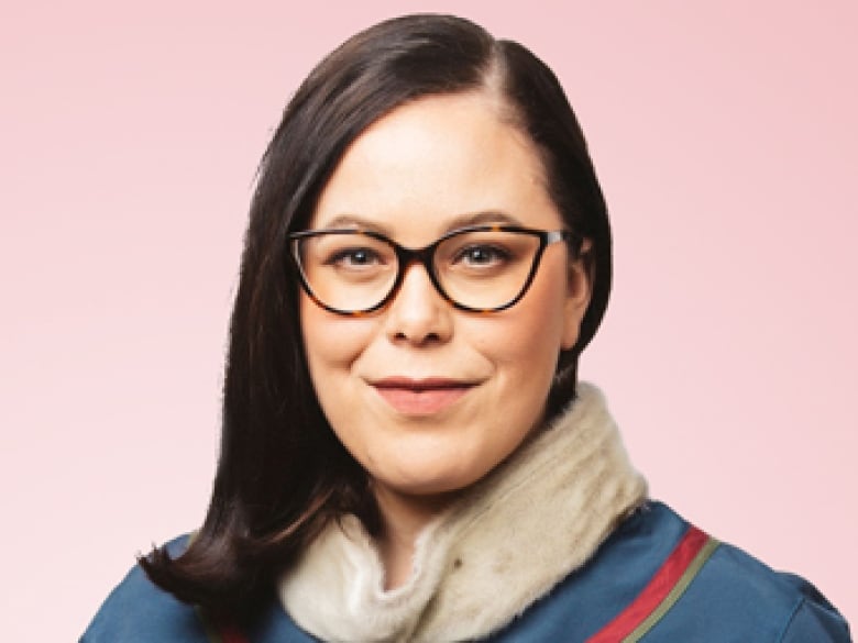 A woman on a salmon background, she wears black glasses and has black hair. 