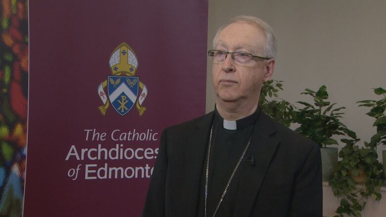 A man wearing glasses stands in front of a banner that says the Catholic Archdioces of Edmonton.