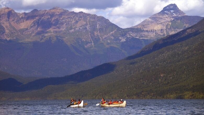 A wide shot of people paddling on two boats in a river, with mountains in the background.