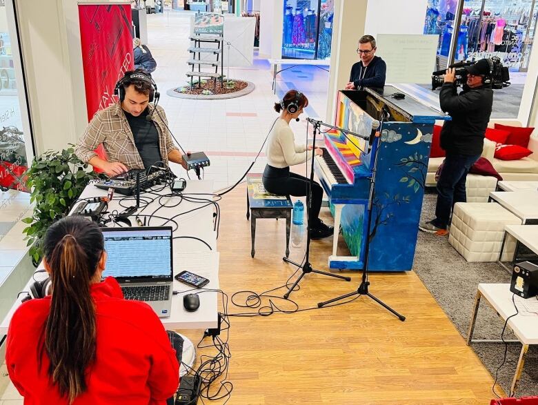 Live radio broadcast, with two people working on sound board and laptop. Pianiast sits at a brightly coloured, upright people as she performs. 