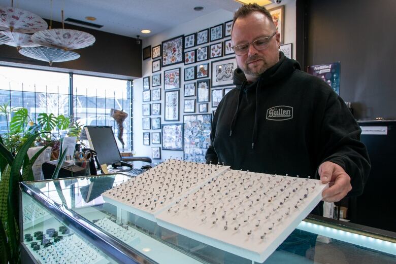 A man displays items in a body piercing shop.