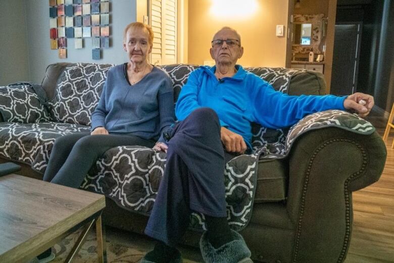 An older man and woman sit on a couch in their living rooms and look into the camera