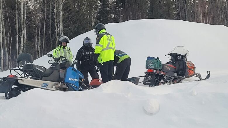 A group of EMS workers in neon yellow jackets huddle around a snowmobile. 