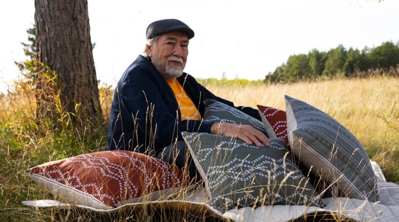 An elderly Indigenous man is pictured in a field with pillows using unique designs.