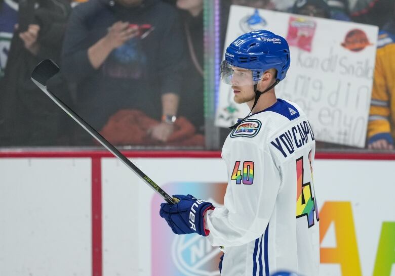 A white hockey player wears a jersey with rainbow lettering on it on the ice.