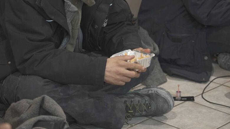 someone holding a hot meal in aluminum container sitting on the floor