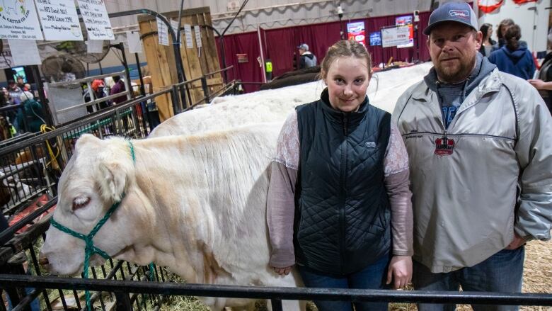 A dad and daughter stand in front of a cow.