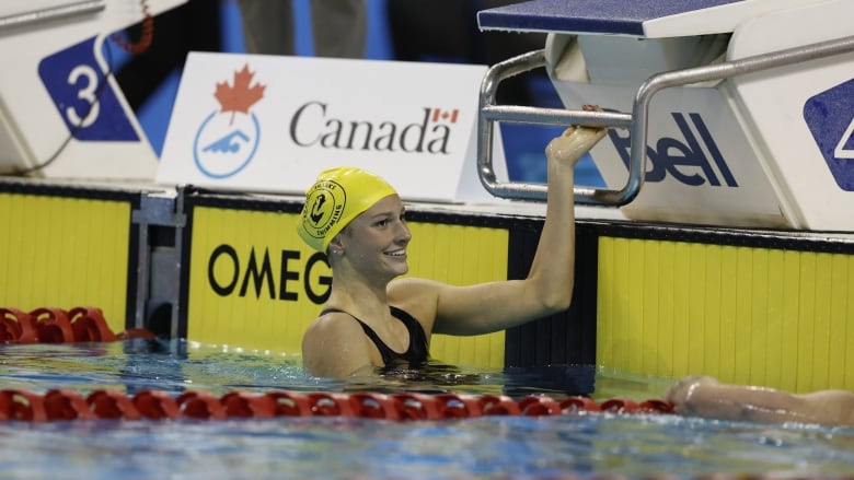 A female swimmer smiles while waiting above water at the end of her lane.