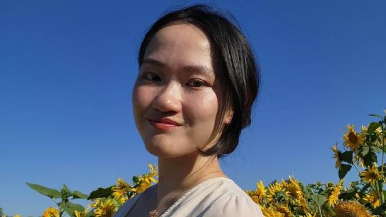 A young Asian woman with short dark hair in front of yellow flowers and a blue sky