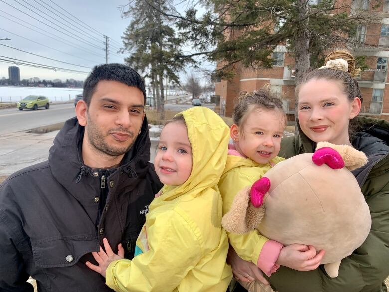 A man and a woman stand near an apartment building with two children.