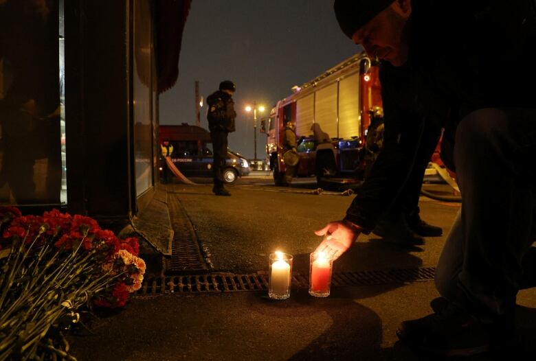 A person lights a candle at a vigil site.