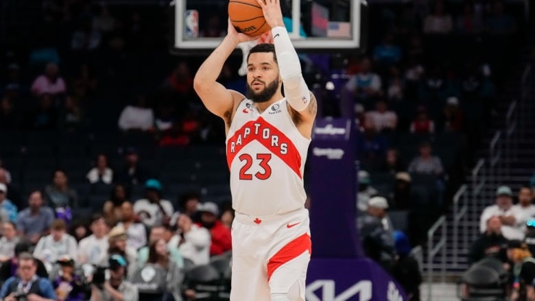 A male basketball player wearing numbers 23 holds the ball over his head with both hands.