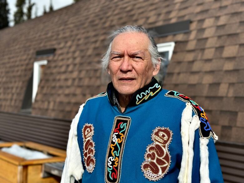 A man is frowning in front of the camera, wearing a blue traditional Indigenous vest. 