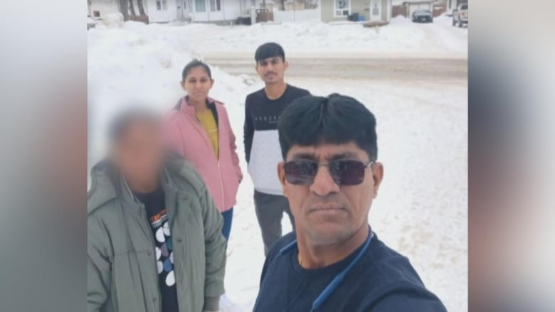 Two men, a woman and a person whose face is blurred out take a selfie in the snow. 