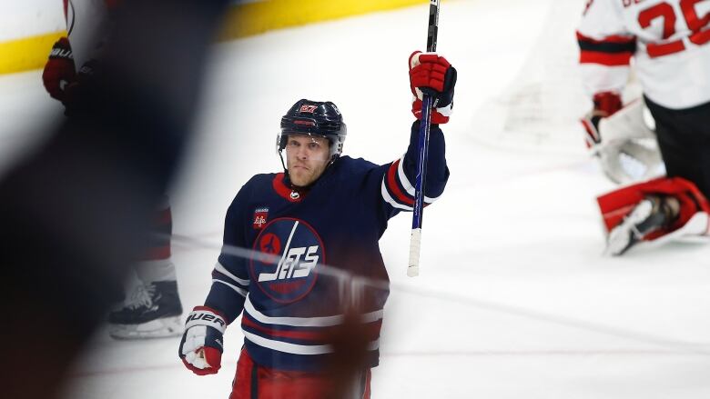 Nikoljah Ehlers wears the Winnipeg Jets reverse retro jersey, which is navy blue, and celebrates a goal with an arm in the frame. 