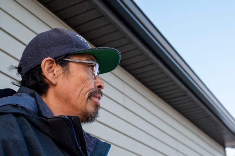 A man wearing a ballcap and glasses looks out into the distance. 