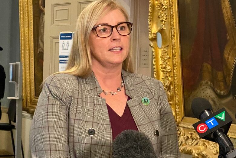 A woman with long hair and glasses speaks into a microphone.