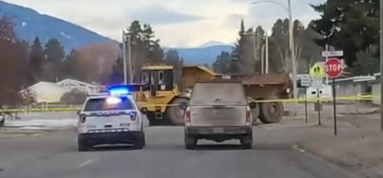 Two police vehicles in front of a large piece of heavy machinery.