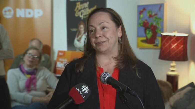 A brown haired woman stands at a microphone