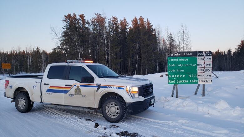 An RCMP truck is parked next to road signs outside of several northern Manitoba First Nation communities.