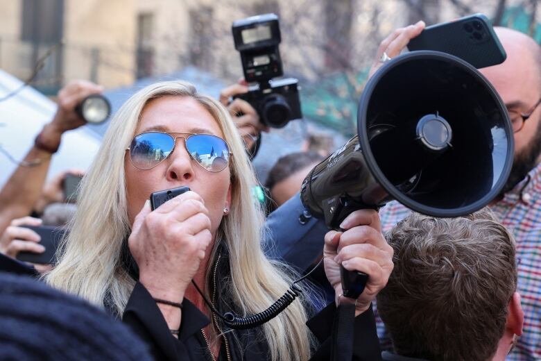 Woman in sunglasses shouting into a megaphone.