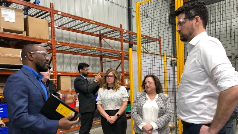 Six people standing in a warehouse, wearing personal protective equipment.