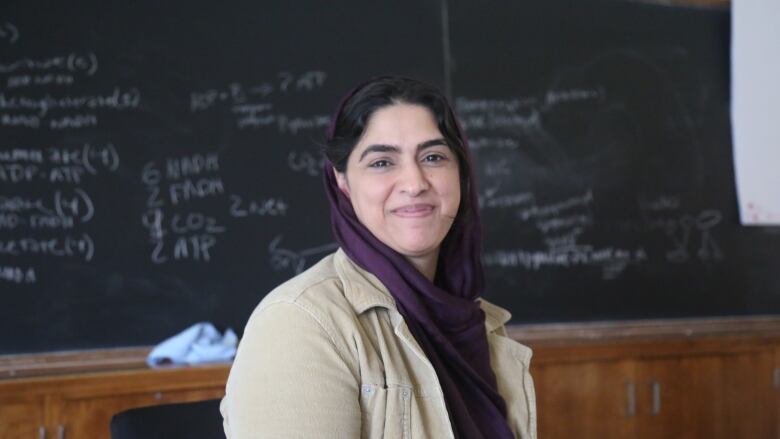 A woman sitting in front of a blackboard smiling at the camera.