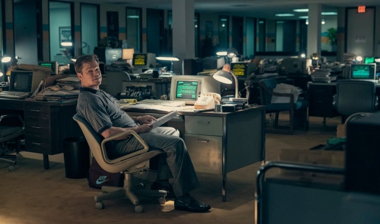 A man sits at a desk in an empty office at night. 