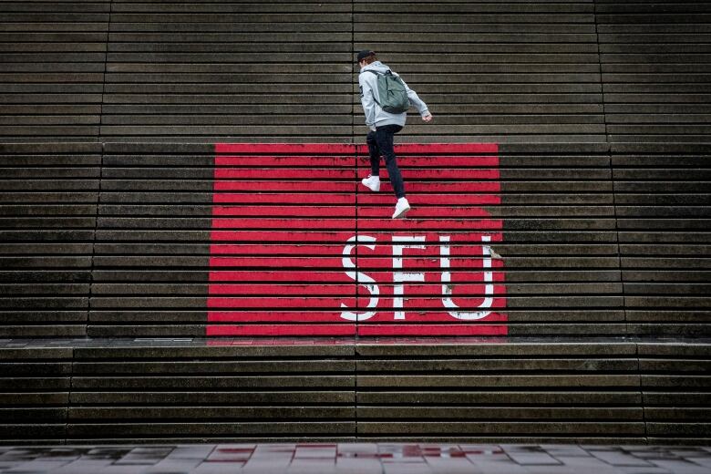 A person in a hoodie walks over steps that have 'SFU' and a red logo painted over in a gradient.