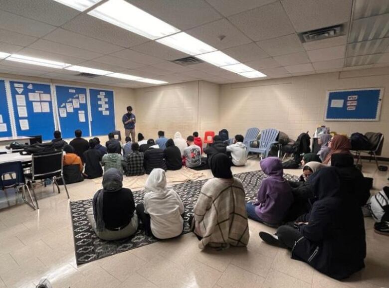 A big group of teenagers sitting on rugs inside a room.