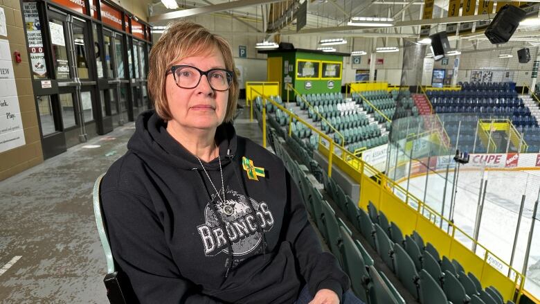 A woman with glasses sits in a hockey arena with a somber look on her face.