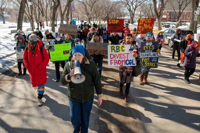 A person with a megaphone leads marchers with signs, including 