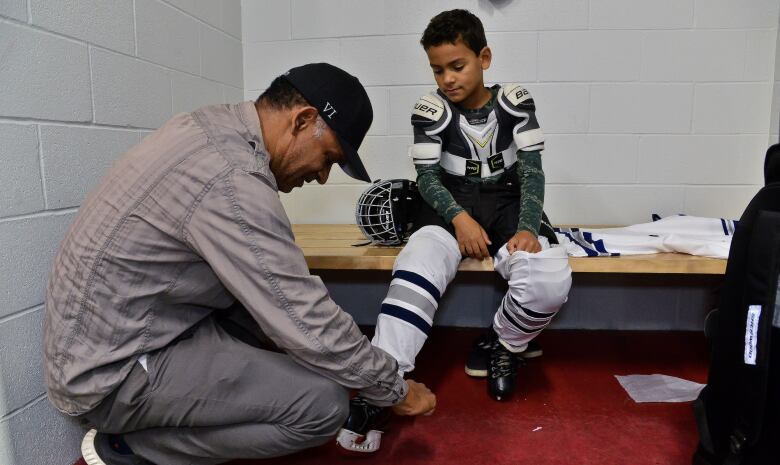 A man crouches down to lace up the skates of a young hockey player.