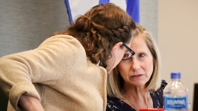 Two women lean in and talk to each other.