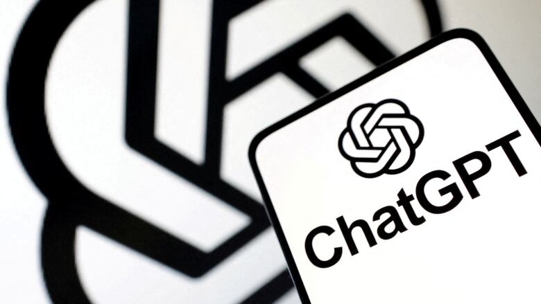 ChatGPT logo over a white background is pictured on a mobile phone held in front of a larger version of the logo.